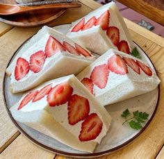 four pieces of cake with strawberries on top sitting on a plate next to a spoon