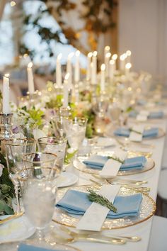 a long table is set with blue and white place settings, silverware, and flowers