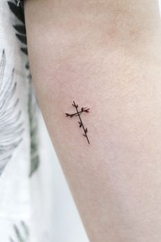 a small cross tattoo on the right arm and leg, with leaves in the background