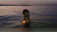 a woman is standing in the water at sunset with her back turned to the camera