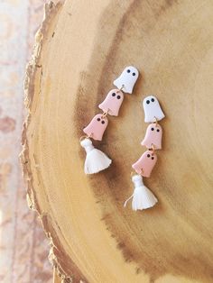 three little ghost charms on a wood slice with white tassels and black eyes