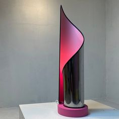 a pink and black vase sitting on top of a white table next to a gray wall