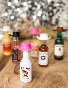 the bottles are lined up on the table with their lids down and one has a pink cowboy hat