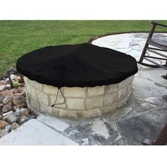 an outdoor fire pit surrounded by rocks and stones with a black cover on it's side