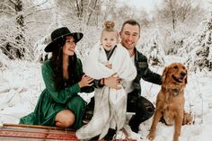 a man, woman and child sitting on a bench in the snow with a dog