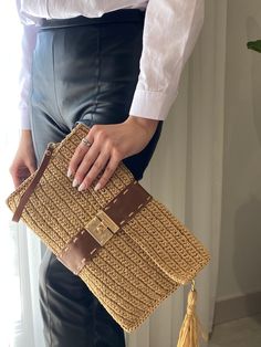 a woman holding a brown and tan woven purse with tassels on the handles