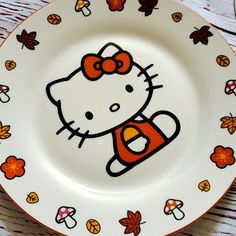 a hello kitty plate sitting on top of a wooden table with autumn leaves around it