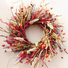 a wreath is hanging on the front door with dried flowers and foliages around it