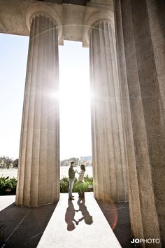 two people are standing in front of some pillars with the sun shining through them and their shadows on the ground