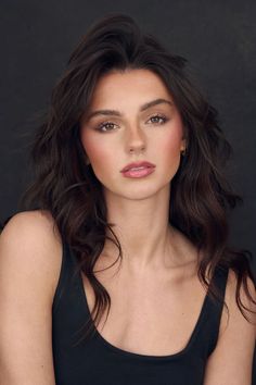 a woman with long dark hair wearing a black tank top and gold hoop earrings is posing for a portrait