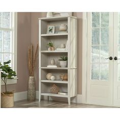 a white bookcase with plants and vases on it in front of a door