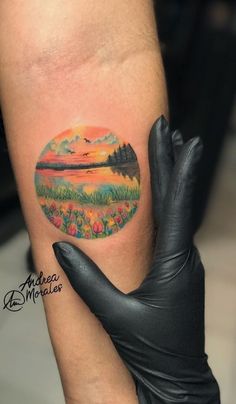 a woman's arm with a tattoo on it that has a sunset in the background