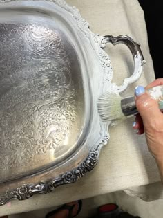 a woman is painting the inside of a silver tray