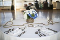 a white table topped with a basket filled with blue and white flowers next to utensils