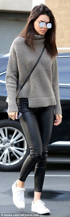 a woman wearing black leather pants and a turtle neck sweater is seen walking down the street