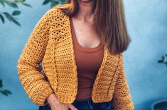 a woman standing in front of a blue wall wearing a yellow crochet cardigan