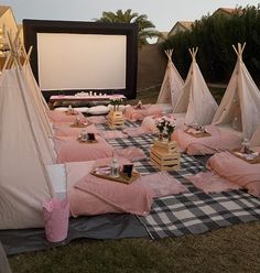 a group of teepee tents sitting on top of a grass covered field next to a movie screen