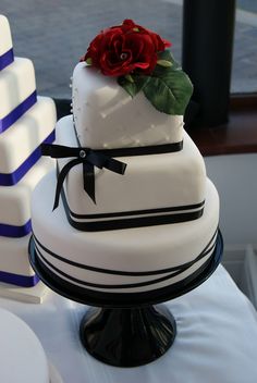 a three tiered cake with a red rose on top and blue stripes around it