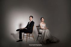 a man and woman sitting on chairs in front of a gray background, posing for the camera