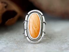 Bold Orange Spiny Oyster Sterling Silver Statement Ring for women. The setting is an oval cabochon 20mm x 10mm that is in a Bezel setting. The 925 Sterling Silver has been fused, stamped and lightly oxidized. This ring has a tapered wide band 1/2" then narrows to 1/8" and cannot be resized. Size 6 The sleek, embellished setting is complemented by a unique tapered chunky silver band, ensuring durability and timeless style. Whether you're shopping for yourself or are searching for the one of a kin Orange Ring, Vero Beach Fl, Statement Ring Silver, Bohemian Rings, Spiny Oyster, Handmade Boho, Wide Bands, Oval Cabochon, Boho Rings