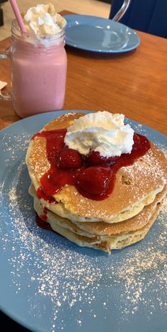 stack of pancakes with whipped cream and strawberry syrup on blue plate next to pink smoothie