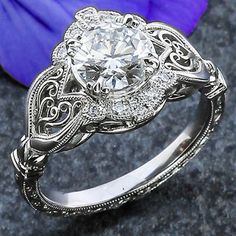 a white gold engagement ring with an intricate filigree design and a round diamond center