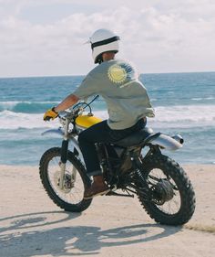 a man riding a dirt bike on top of a sandy beach next to the ocean