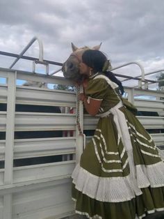 a woman in a green dress leaning against a white fence with a horse's head sticking out