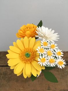 a vase filled with yellow and white flowers on top of a wooden table next to a wall