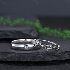 two silver rings with blue topazte stones on a black stone slab next to green plants