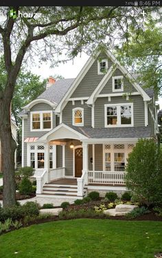 a gray house with white trim and two story windows on the second floor is surrounded by trees