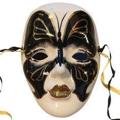 a white mask with black and gold designs on it's face, tied to a yellow ribbon