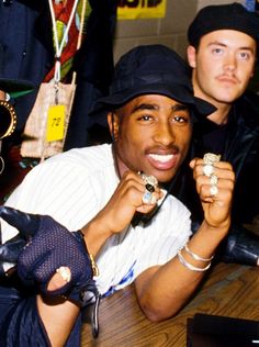 two young men sitting at a table with hats and jewelry on their hands, posing for the camera