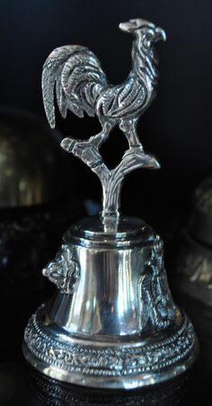 a silver rooster on top of a metal bell