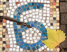 a leaf laying on the ground next to a letter s mosaic tile design with blue, yellow and white tiles