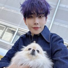 a person with purple hair holding a small dog