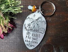 a metal keychain with a quote on it sitting next to some flowers and leaves