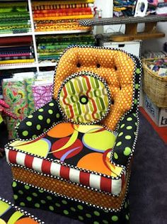 an upholstered chair is in the middle of a room filled with books and fabrics