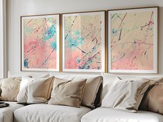 three abstract paintings hang on the wall above a white couch in a living room with beige pillows