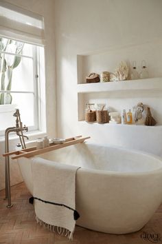 a white bath tub sitting in a bathroom next to a window with shelves above it