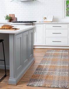 a kitchen with white cabinets and gray island in the center, along with a rug on the floor