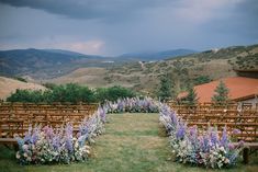 an outdoor ceremony setup with rows of wooden chairs and flowers in the foreground, mountains in the background