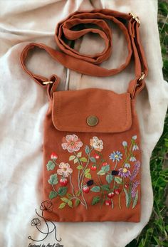 an orange purse sitting on top of a white cloth covered ground with flowers painted on it