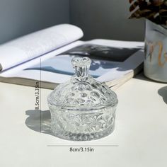 a clear glass jar sitting on top of a table next to a book and vase