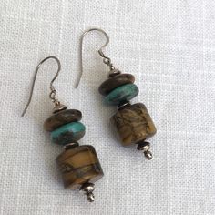 These Tiger Eye N Turquoise stone earrings were designed and created by artist Cheryl Ciaccio for Earth Echos Jewelry. The Grotto earrings are a classic combination of earthy Brown and Blue Color.  Natural blue Turquoise pops in between golden Tiger Eye. The patterns in the Tiger eye are just hypnotic.   The Grotto earrings do have a medium weight feel and dangle 2 inches long. The width is 14mm with the Tiger Eye barrel.    Sterling Silver beads and earwires complete these Earthy Earrings. Brown Natural Stone Drop Earrings, Brown Earrings With Natural Stones And Round Beads, Earthy Drop Earrings With Natural Stones, Earthy Natural Stone Drop Earrings, Artisan Turquoise Earrings With Natural Stones, Artisan Brown Earrings With Natural Stones, Brown Sterling Silver Earrings With Natural Stones, Earthy Turquoise Dangle Earrings, Black Pearl Ring