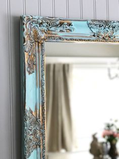 an ornate blue and gold mirror hanging on the wall next to a vase with flowers