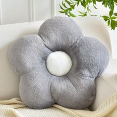 a gray flower shaped pillow sitting on top of a white couch next to a potted plant