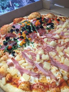 a pizza with ham, pineapples, olives and other toppings in a box