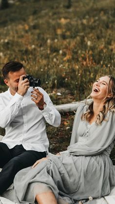 a man and woman sitting next to each other on the ground with a camera in their hands