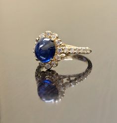 "DeKara Designs Collection Art Deco Inspired Extremely Elegant Halo Opal Diamond Engagement Ring. Metal- 90% Platinum, 10% Iridium. Stones- 1 Natural Oval Cabochon Ceylon Blue Sapphire 2.85 Carats, 26 Round Diamonds F-G Color VS1 Clarity 0.65 Carats. Size- 4-12 An Amazing Art Deco Inspired Ceylon Blue Sapphire Halo Diamond Engagement Ring Made in 18K Yellow Gold. The ring features a beautiful a beautiful Ceylon Blue Sapphire that is Oval in shape and cabochon cut. The sapphire is gracefully set Luxury Hallmarked Oval Cabochon Sapphire Ring, Formal Yellow Gold Cabochon Sapphire Ring, Yellow Gold Sapphire Diamond Ring With Oval Cabochon, Yellow Gold Sapphire Ring With Diamond Oval Cabochon, Luxury Sapphire Cabochon Ring For Anniversary, Luxury Yellow Gold Wedding Ring With Accent Stones, Oval Cabochon Sapphire Ring In Yellow Gold With Diamond, Timeless Blue Oval Cabochon Jewelry, Luxury Yellow Gold Halo Ring With Gemstone